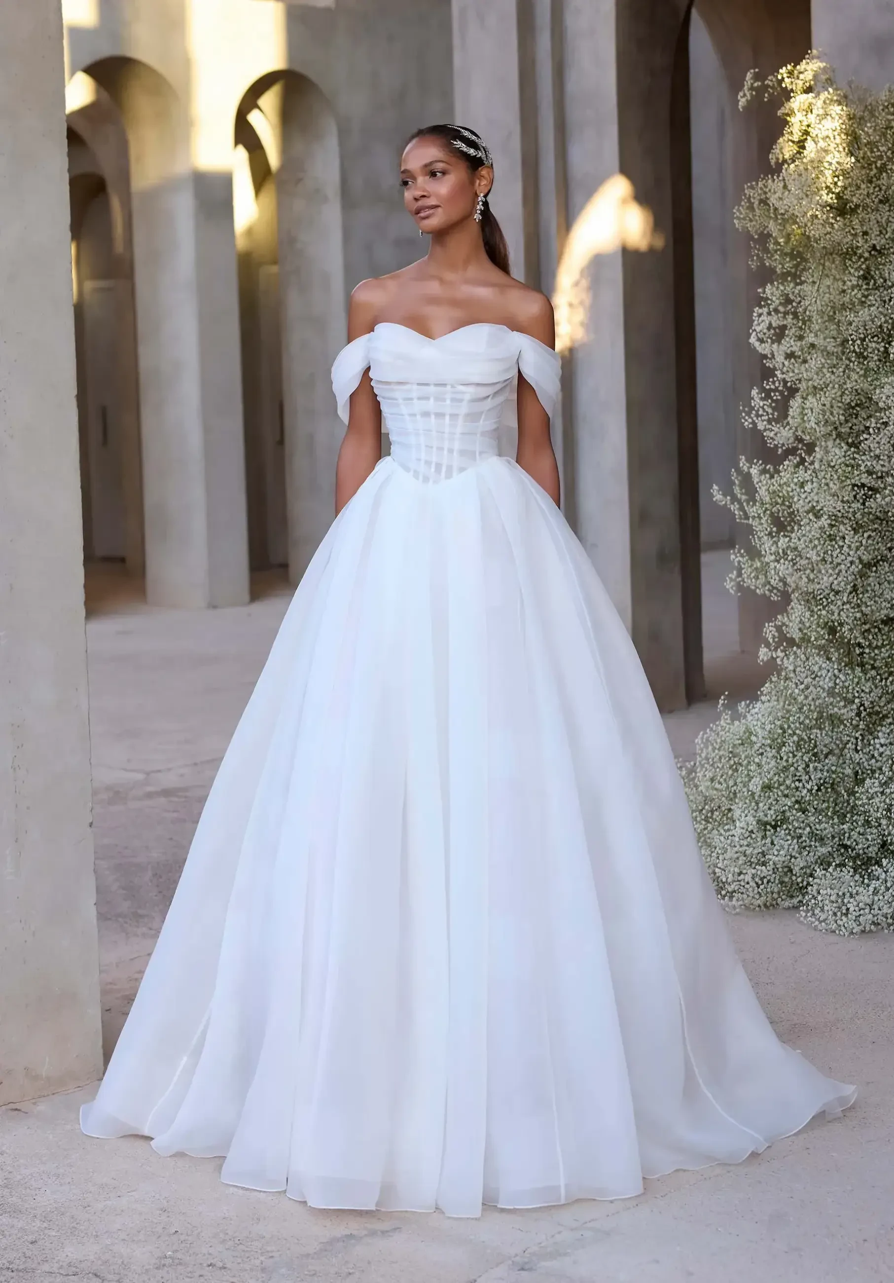 model is wearing an off the shoulder a-line bridal gown with a basque waist